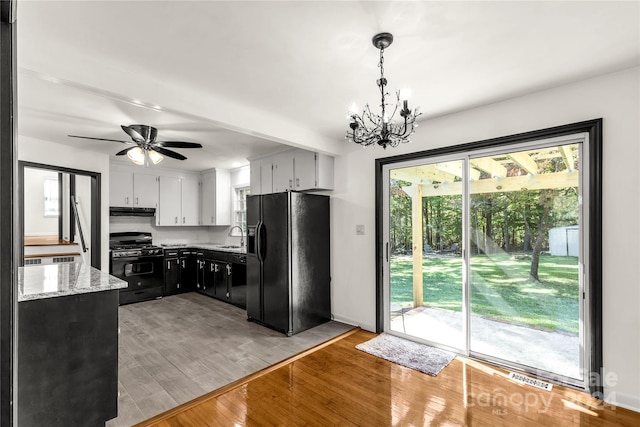 kitchen featuring black appliances, sink, hanging light fixtures, white cabinets, and light hardwood / wood-style flooring