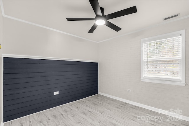 spare room with brick wall, ornamental molding, light wood-type flooring, and ceiling fan