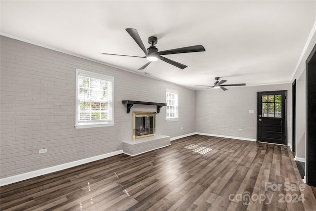 unfurnished living room featuring brick wall, dark wood-type flooring, and plenty of natural light