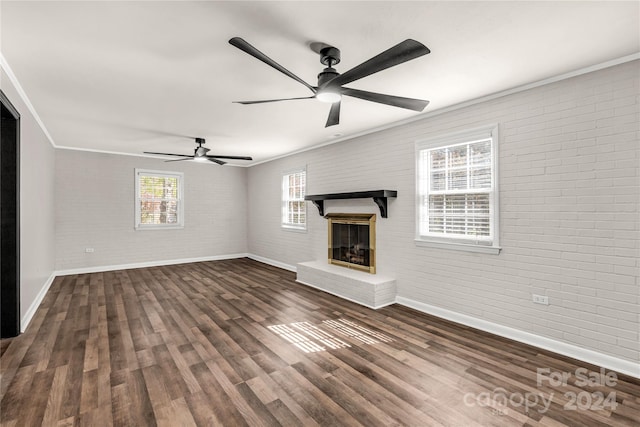 unfurnished living room featuring dark wood-type flooring, brick wall, crown molding, a brick fireplace, and ceiling fan