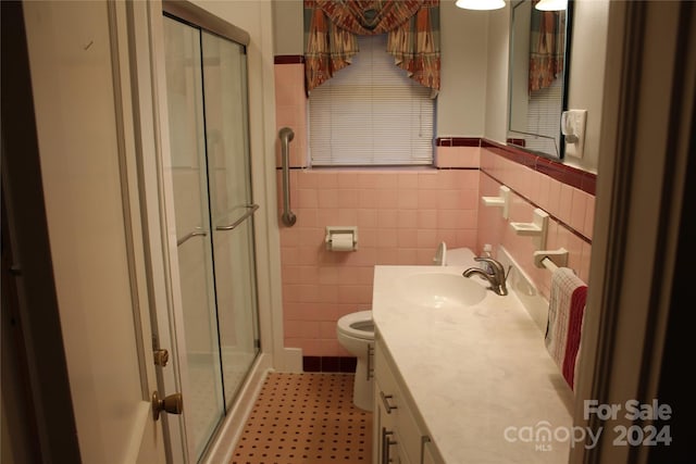 bathroom featuring toilet, a shower with shower door, vanity, and tile walls