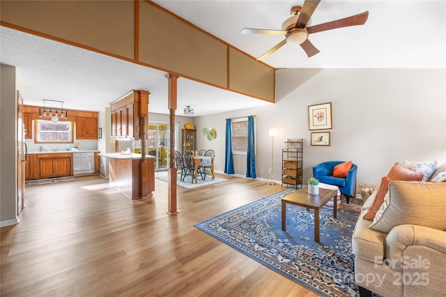 living room with a textured ceiling, vaulted ceiling, light hardwood / wood-style floors, and ceiling fan