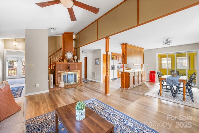 living room featuring a brick fireplace, a high ceiling, ceiling fan, and light wood-type flooring