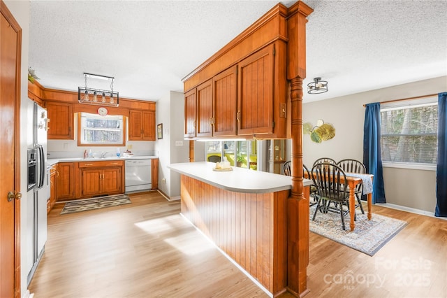 kitchen featuring a kitchen bar, sink, white dishwasher, kitchen peninsula, and light hardwood / wood-style floors