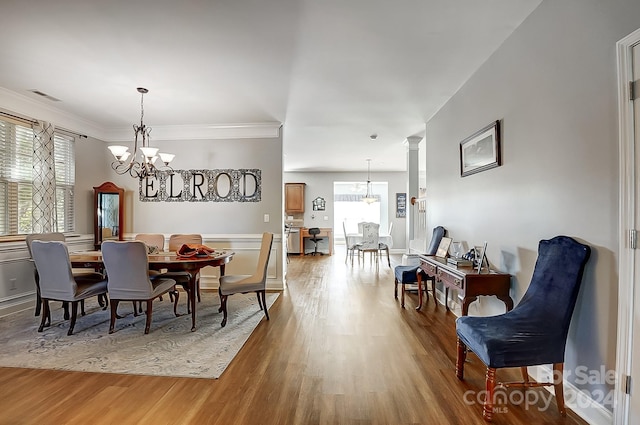 dining room with wood-type flooring, decorative columns, crown molding, and a notable chandelier