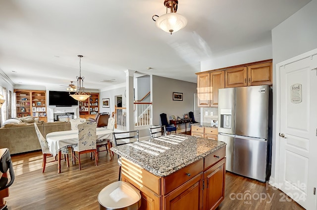 kitchen with dark wood-type flooring, decorative columns, a kitchen island, dark stone countertops, and stainless steel fridge