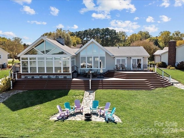 back of property with a fire pit, a sunroom, and a lawn