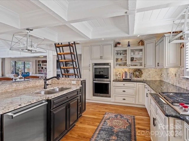 kitchen featuring beam ceiling, appliances with stainless steel finishes, light hardwood / wood-style flooring, pendant lighting, and sink