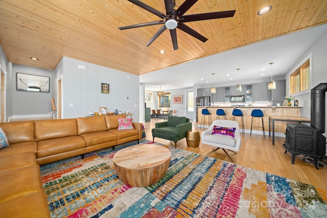 living room with wood ceiling, light wood-type flooring, a wood stove, and ceiling fan