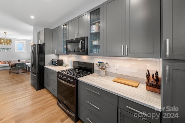 kitchen with gray cabinetry, tasteful backsplash, black appliances, light hardwood / wood-style floors, and light stone counters