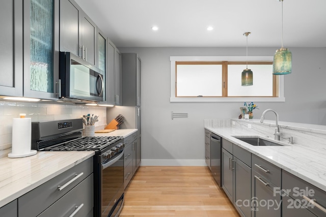 kitchen featuring appliances with stainless steel finishes, light stone countertops, light wood-type flooring, pendant lighting, and sink