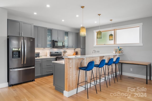 kitchen with hanging light fixtures, backsplash, a kitchen bar, light hardwood / wood-style floors, and stainless steel appliances