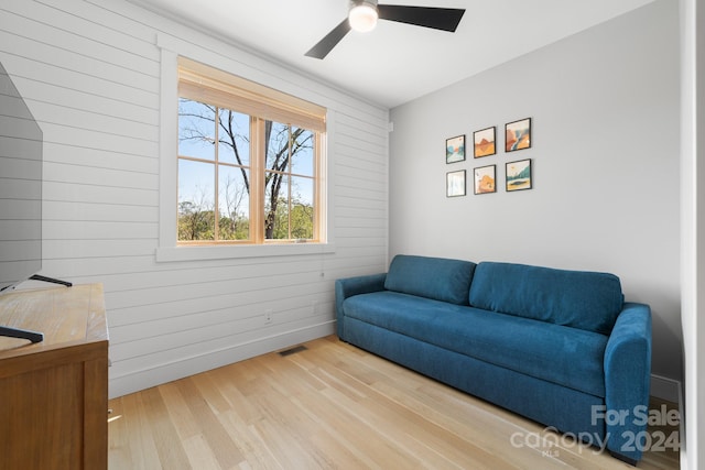 sitting room featuring wooden walls, light wood-type flooring, and ceiling fan