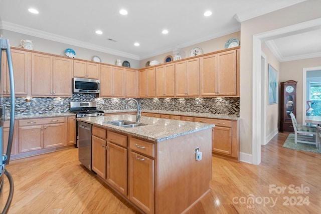 kitchen with light stone counters, stainless steel appliances, sink, light hardwood / wood-style flooring, and an island with sink