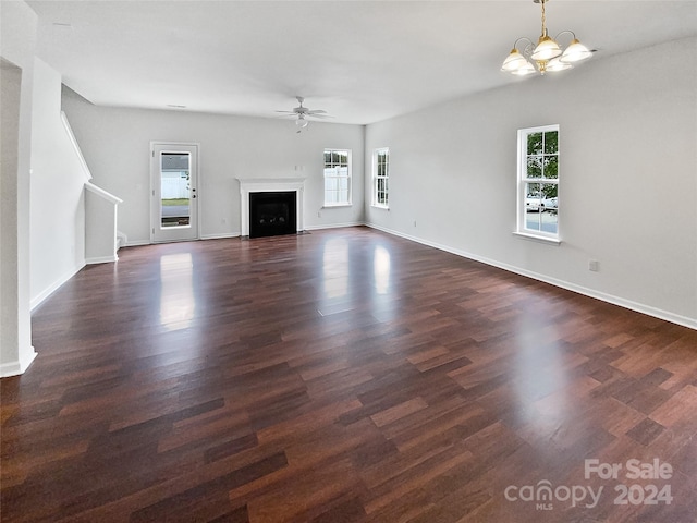 unfurnished living room with dark wood-type flooring, ceiling fan with notable chandelier, and plenty of natural light