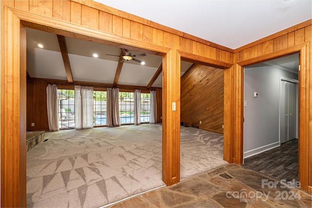 interior space with wooden walls, lofted ceiling with beams, dark colored carpet, and ceiling fan