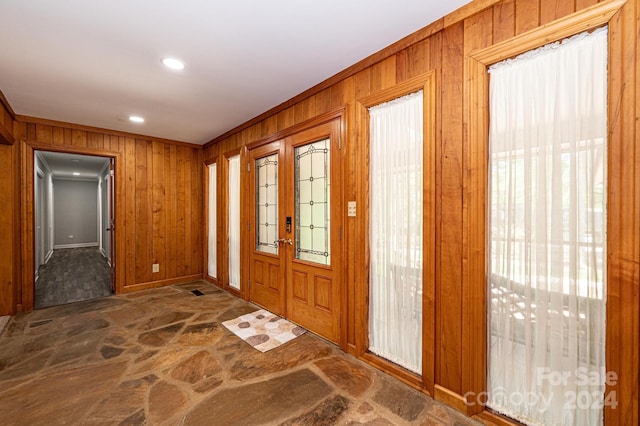 foyer entrance with ornamental molding, french doors, a healthy amount of sunlight, and wooden walls