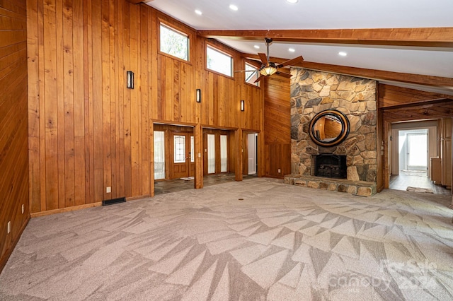 unfurnished living room featuring a stone fireplace, wooden walls, lofted ceiling with beams, light colored carpet, and ceiling fan