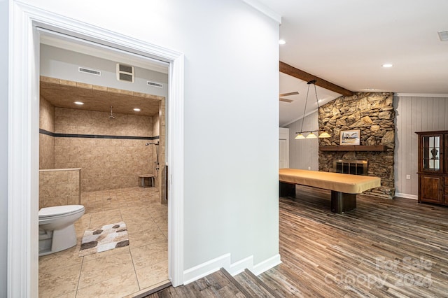 bathroom featuring vaulted ceiling with beams, a stone fireplace, toilet, walk in shower, and hardwood / wood-style flooring