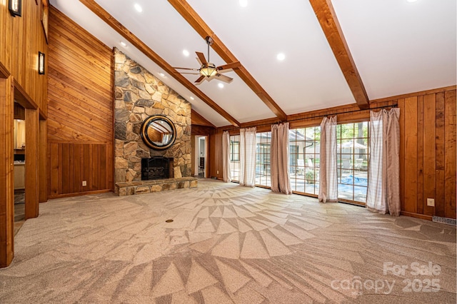 unfurnished living room with a stone fireplace, high vaulted ceiling, wood walls, light colored carpet, and beam ceiling