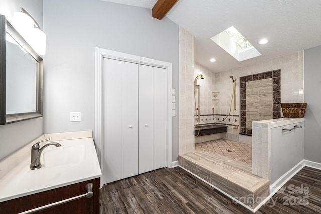 bathroom with vanity, wood-type flooring, lofted ceiling with skylight, and a tile shower