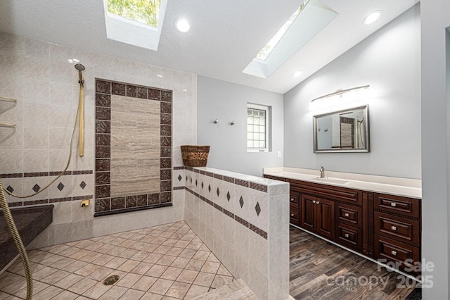 bathroom featuring vanity, hardwood / wood-style flooring, vaulted ceiling with skylight, and tiled shower