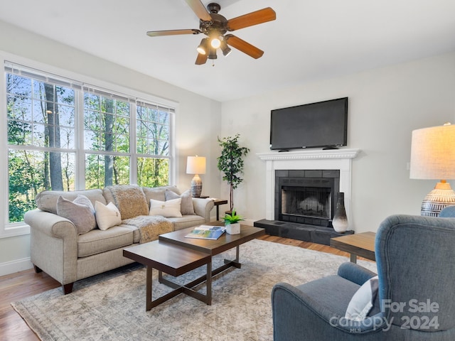 living room with ceiling fan, a tile fireplace, a healthy amount of sunlight, and light hardwood / wood-style flooring