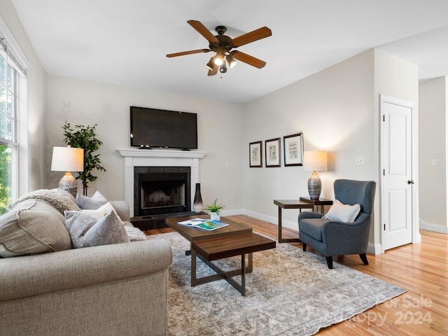 living room with a tiled fireplace, wood-type flooring, and ceiling fan