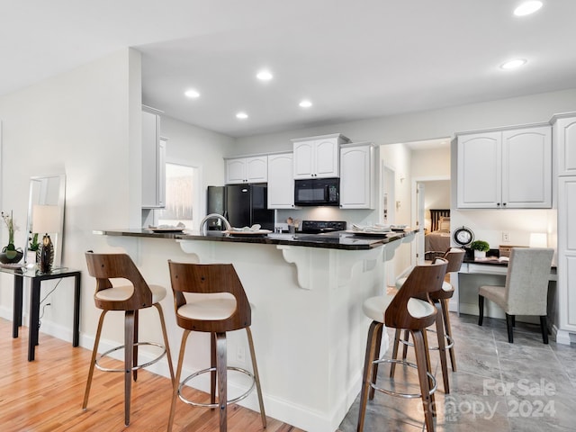 kitchen with white cabinetry, kitchen peninsula, black appliances, and a breakfast bar