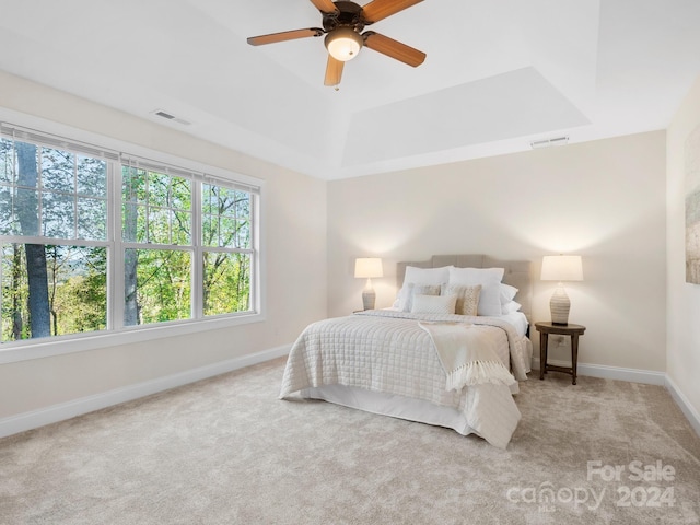 bedroom with light colored carpet, ceiling fan, and a raised ceiling