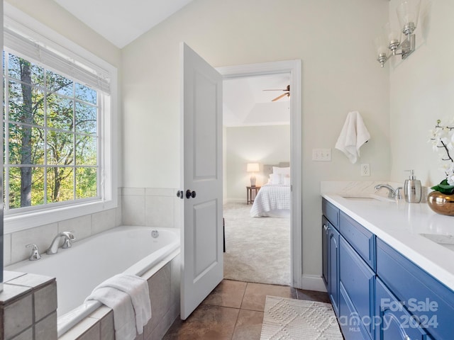 bathroom with a relaxing tiled tub, ceiling fan, vanity, and tile patterned floors