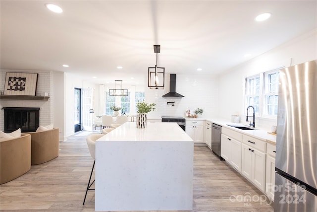 kitchen with white cabinets, hanging light fixtures, appliances with stainless steel finishes, wall chimney exhaust hood, and sink