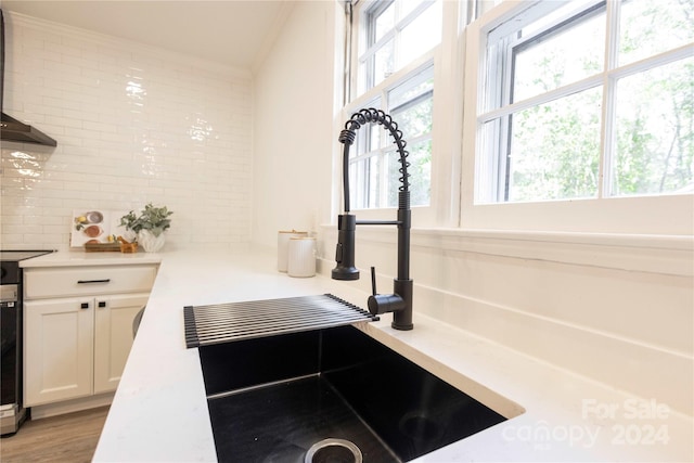 details featuring wall chimney exhaust hood, stainless steel stove, sink, white cabinetry, and light hardwood / wood-style floors