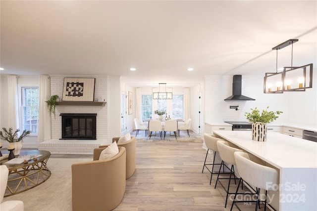 living room with light hardwood / wood-style floors, a brick fireplace, an inviting chandelier, and a wealth of natural light