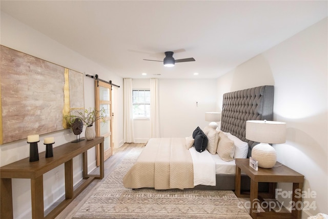 bedroom featuring ceiling fan, light hardwood / wood-style floors, and a barn door