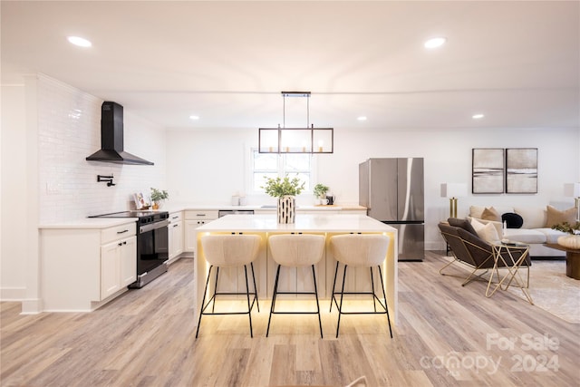 kitchen with wall chimney range hood, appliances with stainless steel finishes, light hardwood / wood-style floors, white cabinets, and a breakfast bar area