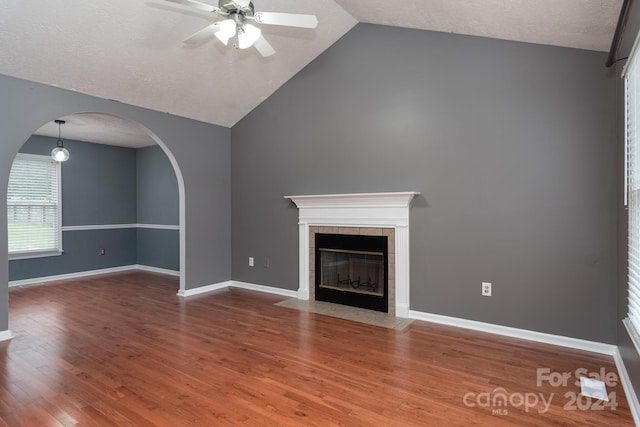 unfurnished living room featuring a tile fireplace, hardwood / wood-style floors, vaulted ceiling, a textured ceiling, and ceiling fan