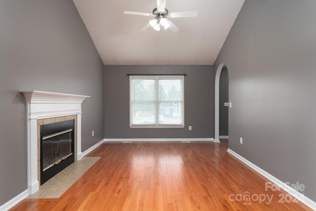 unfurnished living room featuring a tile fireplace, vaulted ceiling, light hardwood / wood-style floors, and ceiling fan