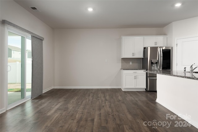 kitchen featuring white cabinets, stainless steel refrigerator with ice dispenser, dark stone counters, and plenty of natural light