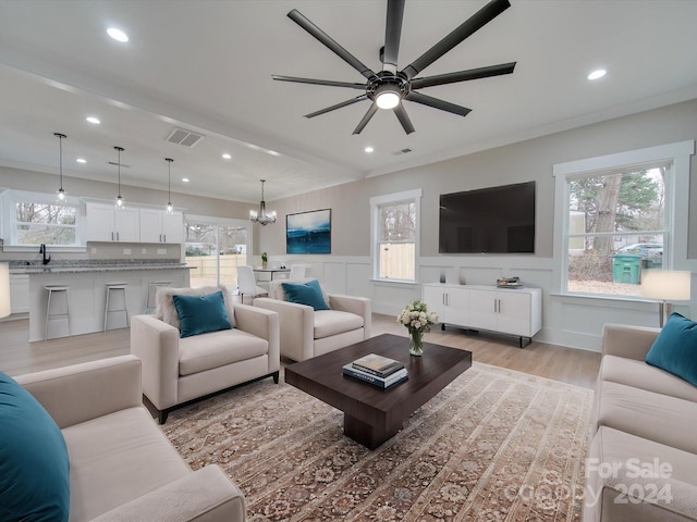 living room featuring ceiling fan with notable chandelier, light hardwood / wood-style floors, crown molding, and sink