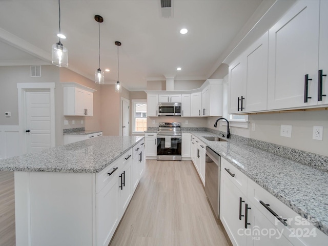 kitchen featuring light stone countertops, stainless steel appliances, a kitchen island, white cabinets, and light wood-type flooring