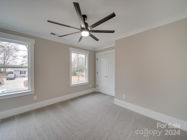 unfurnished bedroom featuring multiple windows, light colored carpet, ceiling fan, and crown molding