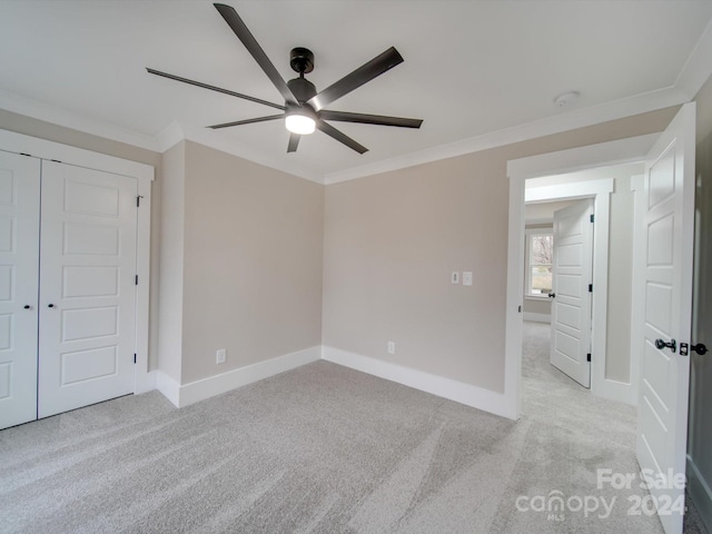 unfurnished bedroom featuring a closet, light colored carpet, ceiling fan, and crown molding