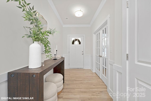 entryway with light wood-type flooring, ornamental molding, french doors, wainscoting, and a decorative wall