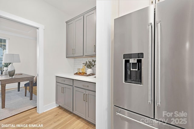 kitchen featuring light wood-type flooring, stainless steel refrigerator with ice dispenser, decorative backsplash, and gray cabinetry