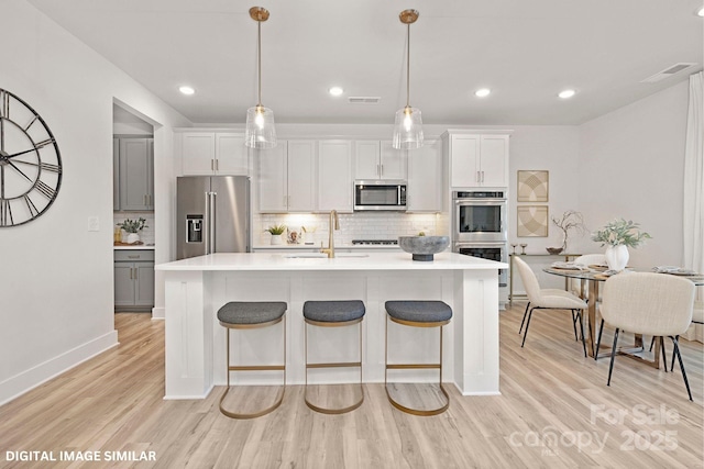 kitchen featuring a kitchen island with sink, stainless steel appliances, a sink, and light countertops