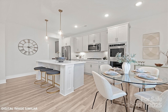 kitchen featuring stainless steel appliances, tasteful backsplash, light wood-type flooring, and a kitchen island with sink