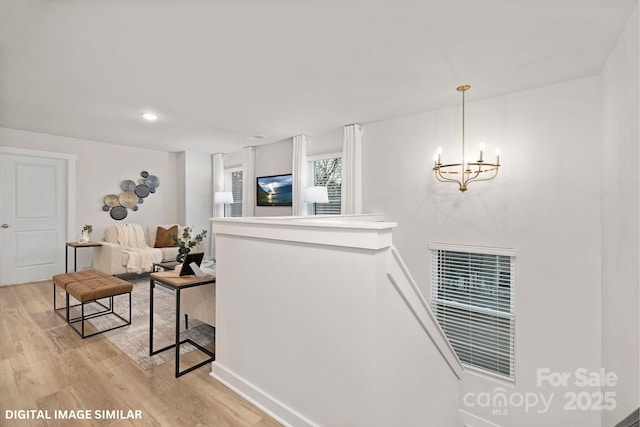 hall featuring visible vents, light wood-style flooring, an upstairs landing, and a notable chandelier