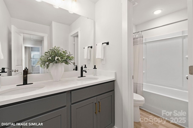 full bathroom featuring wood finished floors, a sink, toilet, and double vanity