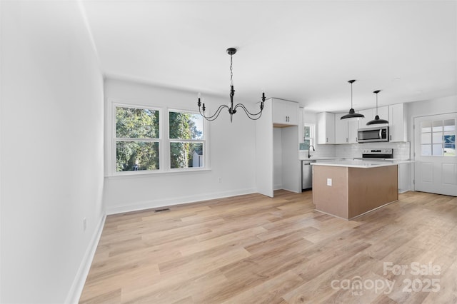 kitchen featuring a center island, light countertops, decorative backsplash, appliances with stainless steel finishes, and light wood-style floors